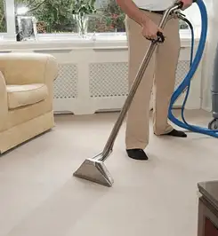 Professional carpet cleaner using a hot-water extraction wand and hose machine in a living room in Lakewood, CO.