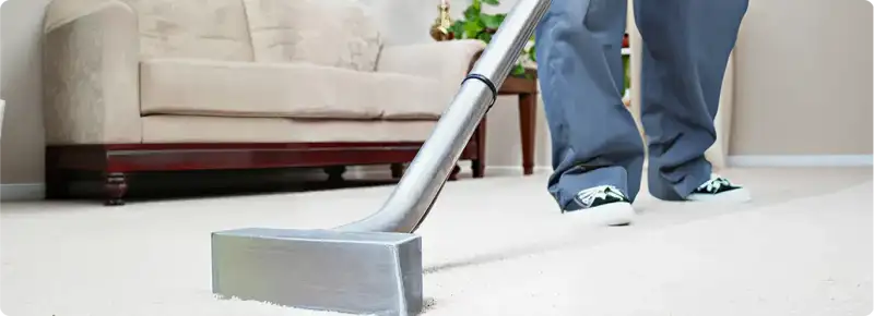 Carpet cleaning technician using a hot-water extraction wand on a light-colored carpet in a living room, Lakewood, CO.