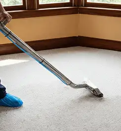 Steam carpet cleaning technician using a hot-water extraction wand on a residential carpet, wearing blue protective shoe covers Lakewood, CO.